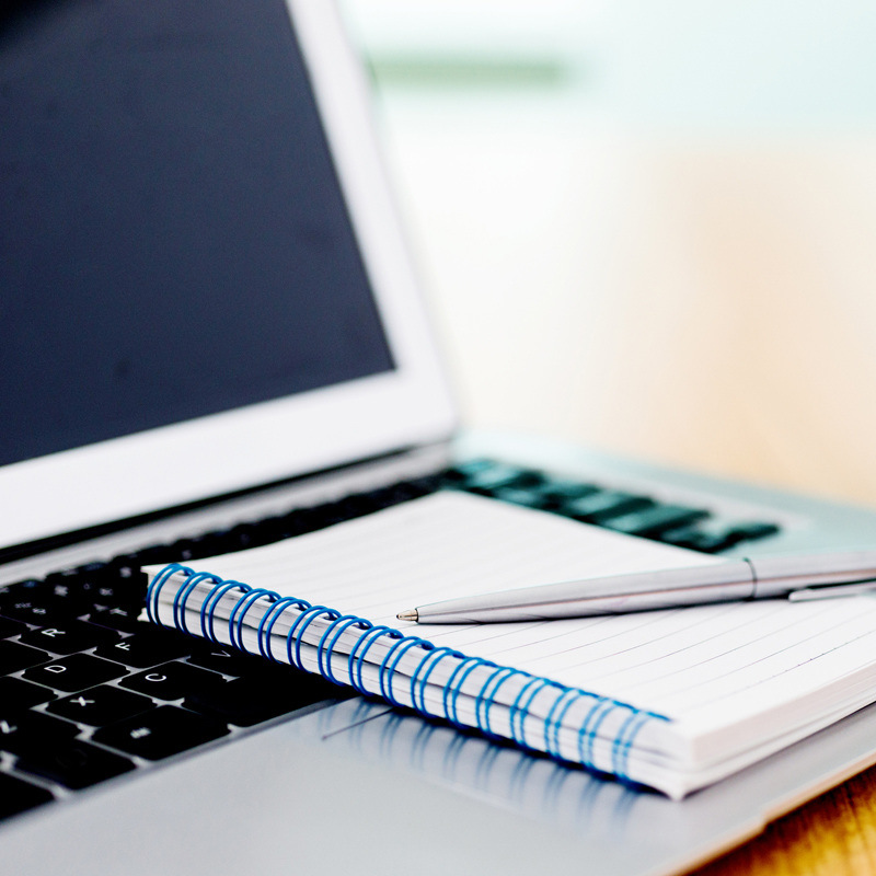 Laptop with pen and spiral notebook on desk.