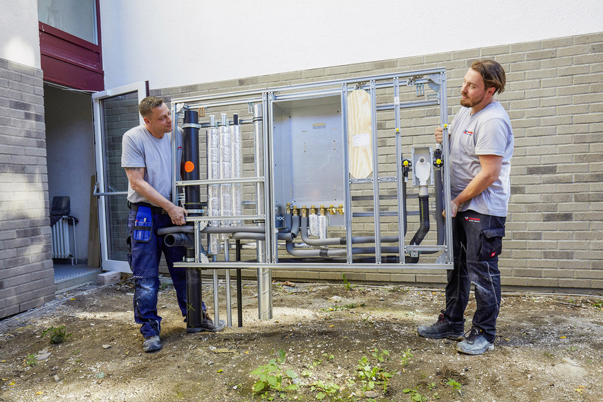 Die einzelnen Einheiten der Installationswand werden von zwei Installateuren in die jeweilige Wohnung getragen.