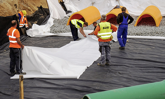 Unterirdisches Retentionssystem mit schwarzer PEHD-Folie, darauf Geotextil und Schottermaterial als Grundlage für die Birco-Rigolentunnel von Stormtech