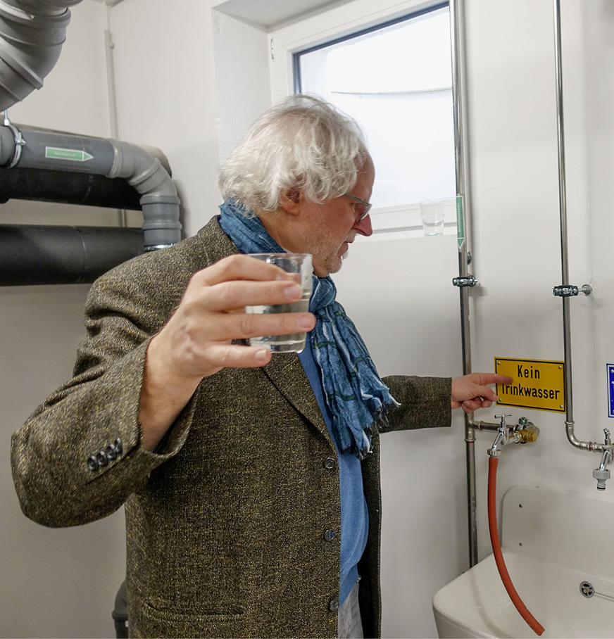 Probenahme im Technikraum durch den Planer Erwin Nolde. Das Betriebswasser aus dem aufbereiteten Grauwasser ist weder durch Geruch noch Optik vom Trinkwasser zu unterscheiden. Es passiert zum Abschluss der Reinigung einen Sandfilter und die UV-Desinfektion. Verwendung hier: Toilettenspülung.