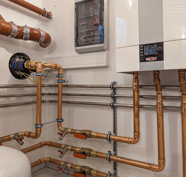 Bei der Elektroinstallation kann Zeit für die Montage und Abstimmung gespart werden, wenn eine Wolf Wärmepumpen-Unterverteilung eingebaut wird. Links im Bild: Die Innenansicht der Wolf Wanddurchführung und die Inneneinheit der Wolf CHA.