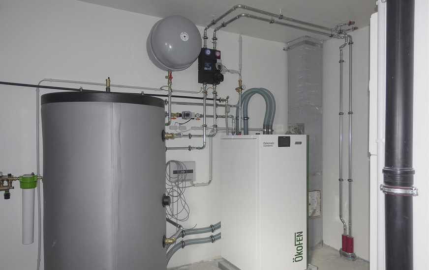 Brennwert-Holzpelletkessel des Herstellers ÖkoFEN. Links Pufferspeicher für das erwärmte Heizungswasser, um die Anzahl der Brennerstarts zu senken. Die Dämmung der Rohre erfolgte im zeitlichen Anschluss.