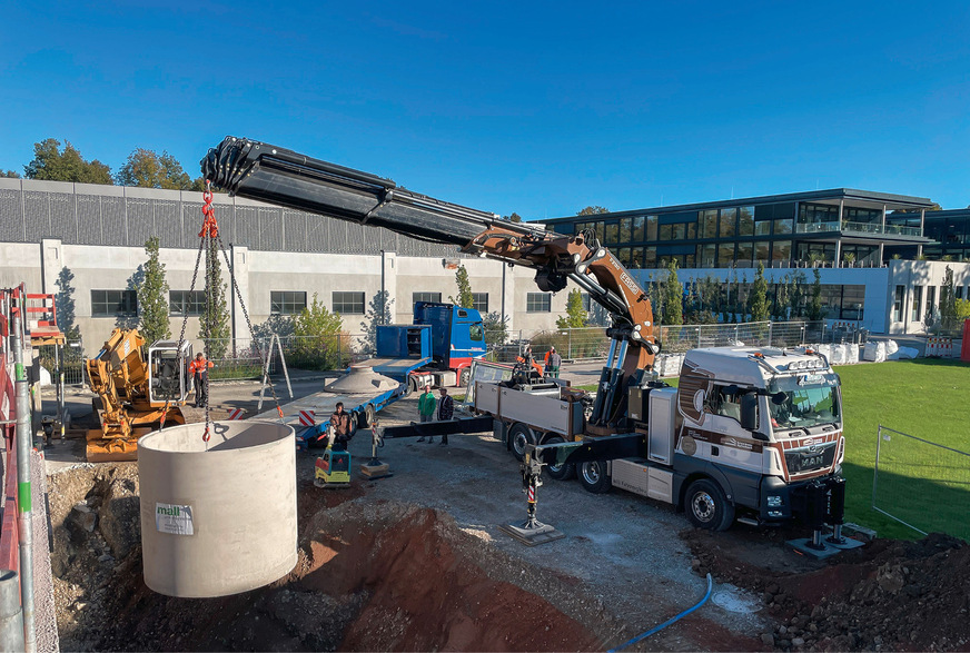 Versetzen der Regenspeicher vom Kran des Lieferfahrzeugs in die vorbereitete Baugrube. Fünf Betonbehälter, die untereinander verbunden sind, bilden die sogenannte Mehrbehälteranlage, der ein Filterschacht vorgeschaltet wurde. Dieser reinigt das vom Dach kommende Regenwasser.