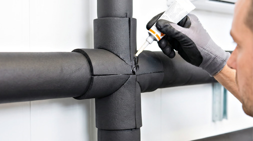 Bei Kälte-, Klima- und Soleleitungen reicht die richtige Dämmstoffdicke allein nicht aus. Die luftdichte Außenhaut – hier beim sorgfältigen Verkleben einer Naht an einer Elastomerschaum-Dämmung – hält feuchte Raumluft zuverlässig von der kalten Rohroberfläche fern.