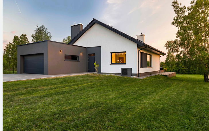Alt-Text-Vorschlag (optimiert für die Zielgruppe und das Themenfeld): „Einfamilienhaus mit moderner Gas-Brennwertheizung, auffälliger schwarzer Dacheindeckung und sichtbarem Abluftkamin; im Vordergrund eine Außeneinheit für die Wohnraumlüftung – typische Installationsbeispiele aus der SHK-Praxis“. - © Bild: Glen Dimplex