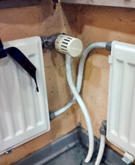 Zwei weiße Heizkörper, die durch Rohre miteinander verbunden sind, in der Ecke eines Zimmers mit pfirsichfarbenen Wänden.