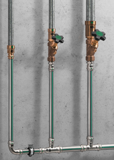 Zwei vertikale Metallrohre mit Messingventilen und grünen Griffen sind an einer grauen Betonwand angebracht. - © Bild: Viega