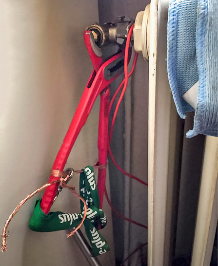 Rote Rohrzange, die an ein Heizkörperventil geklemmt und mit einer Schnur und einem Draht gesichert ist, neben einem blauen Handtuch.