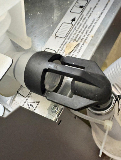 Nahaufnahme eines schwarzen Kunststoffschlauchs, der an einer Maschine befestigt ist, wobei die beschrifteten Anweisungen sichtbar sind.